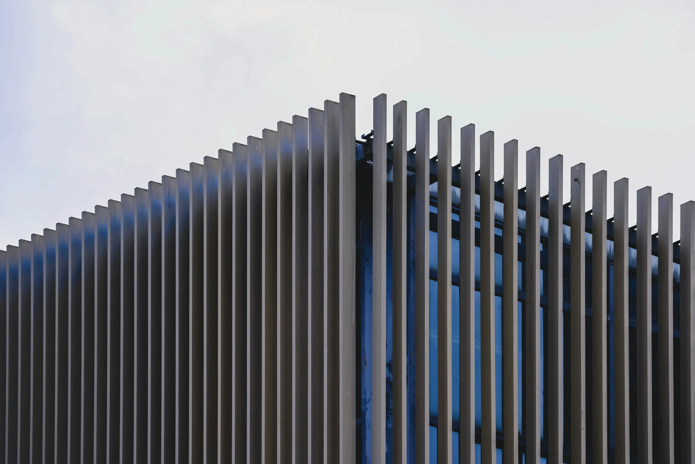 Modern dark aluminium slat boundary fence against a clear sky