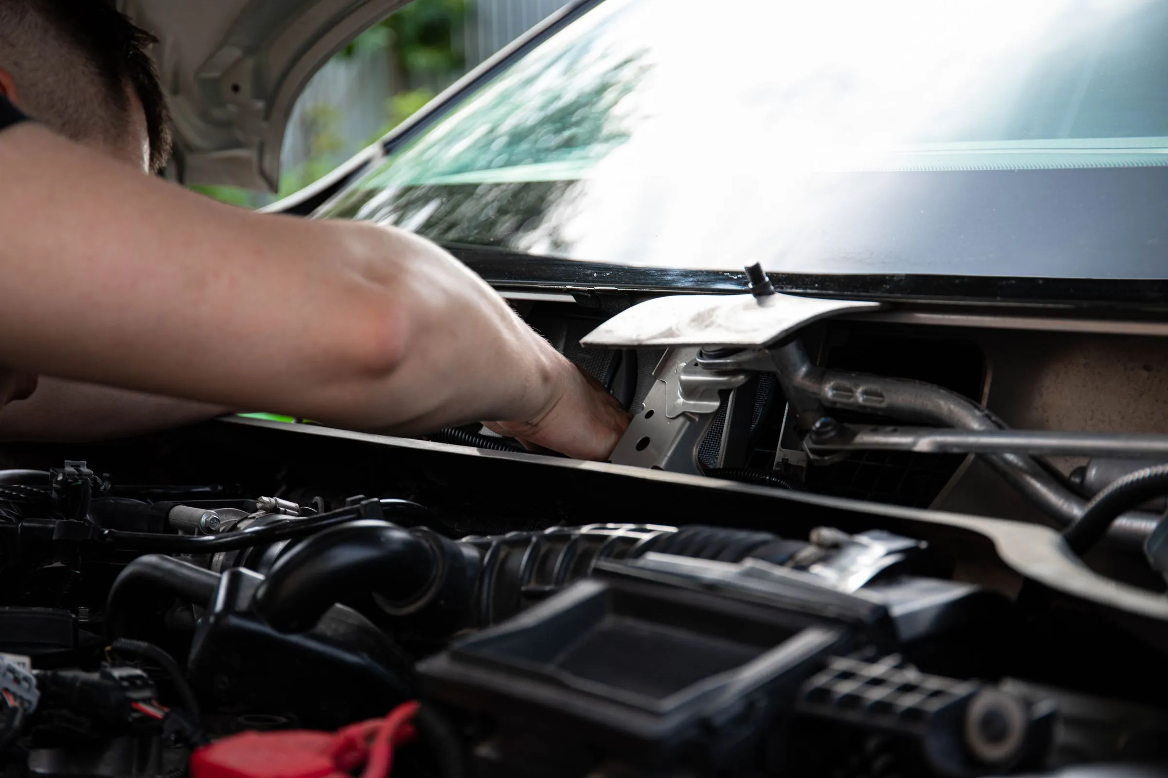 Mechanic working under the open bonnet of a car outdoors