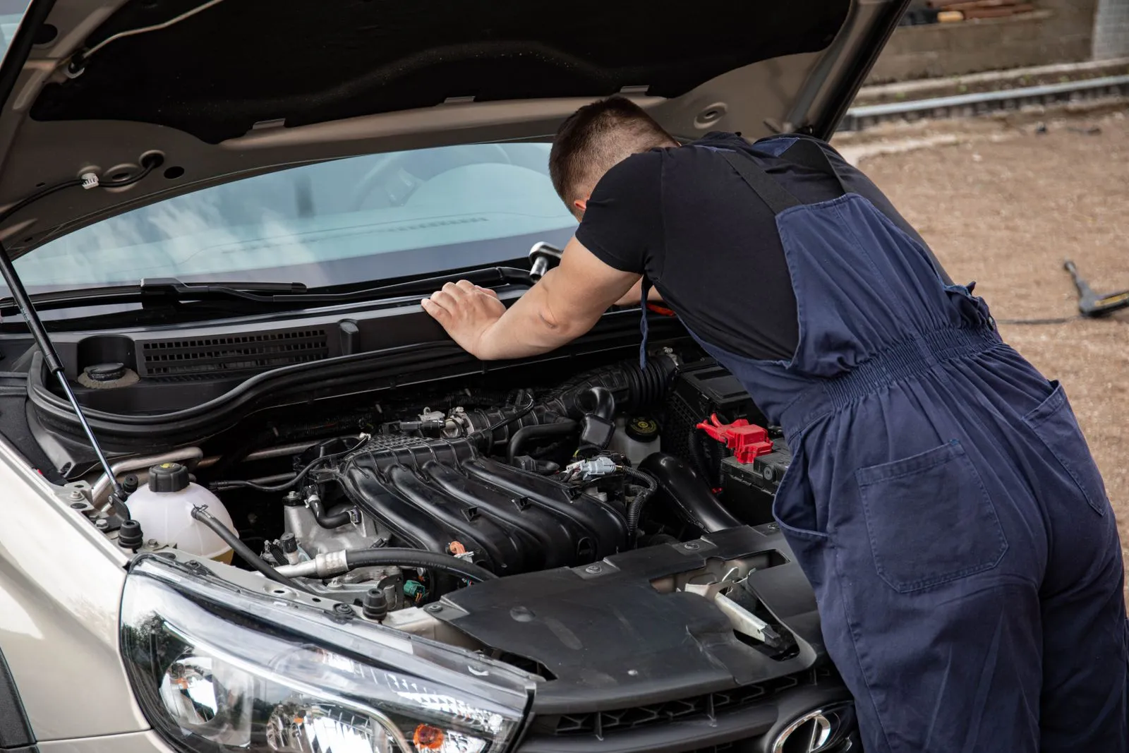 Mechanic in overalls servicing a car with the bonnet up, outdoors