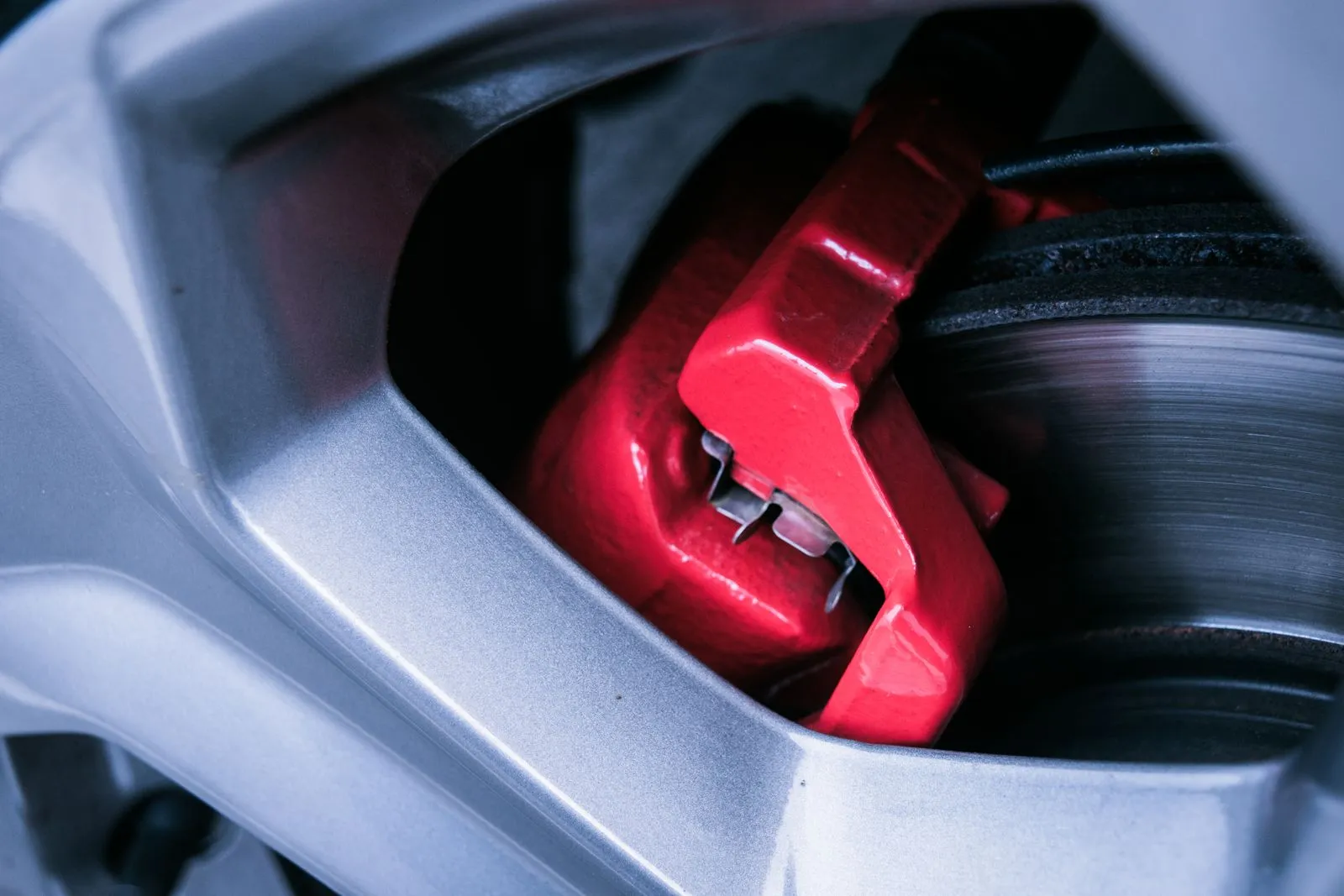 Close-up of a red brake caliper and disc rotor behind an alloy wheel