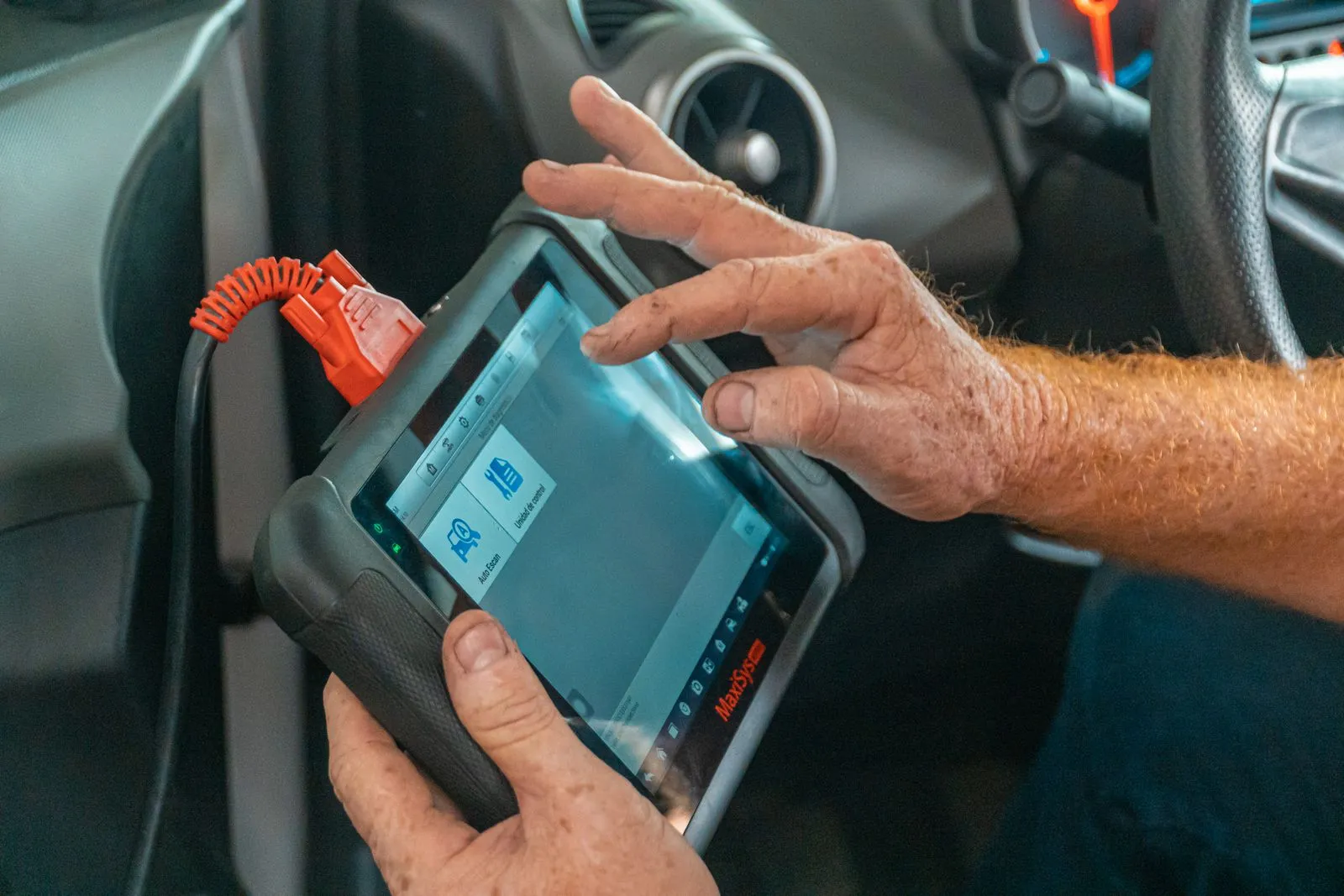 Mechanic using a handheld diagnostic scan tool inside a car