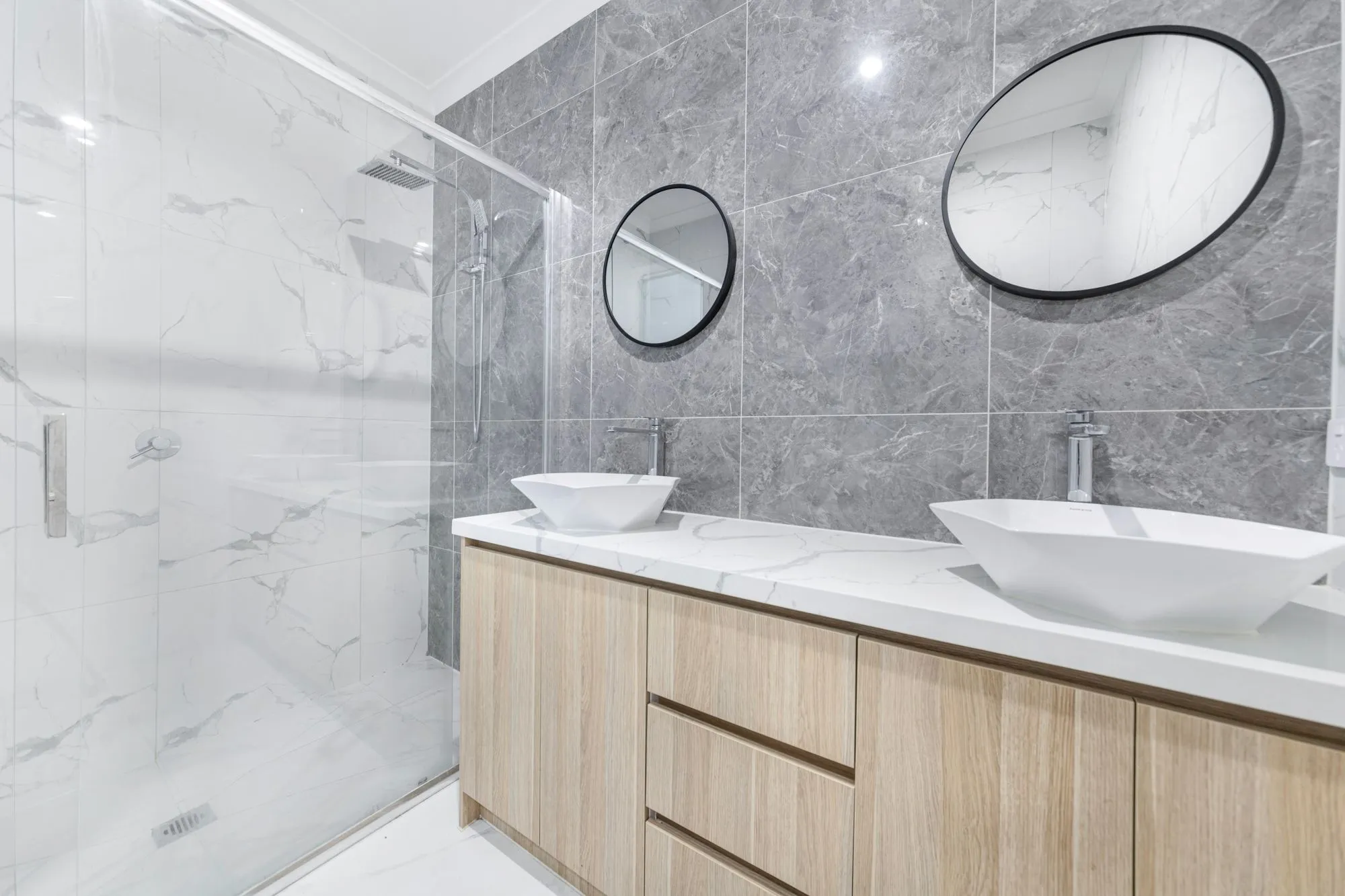 A finished ensuite with marble walls, timber joinery and warm lighting