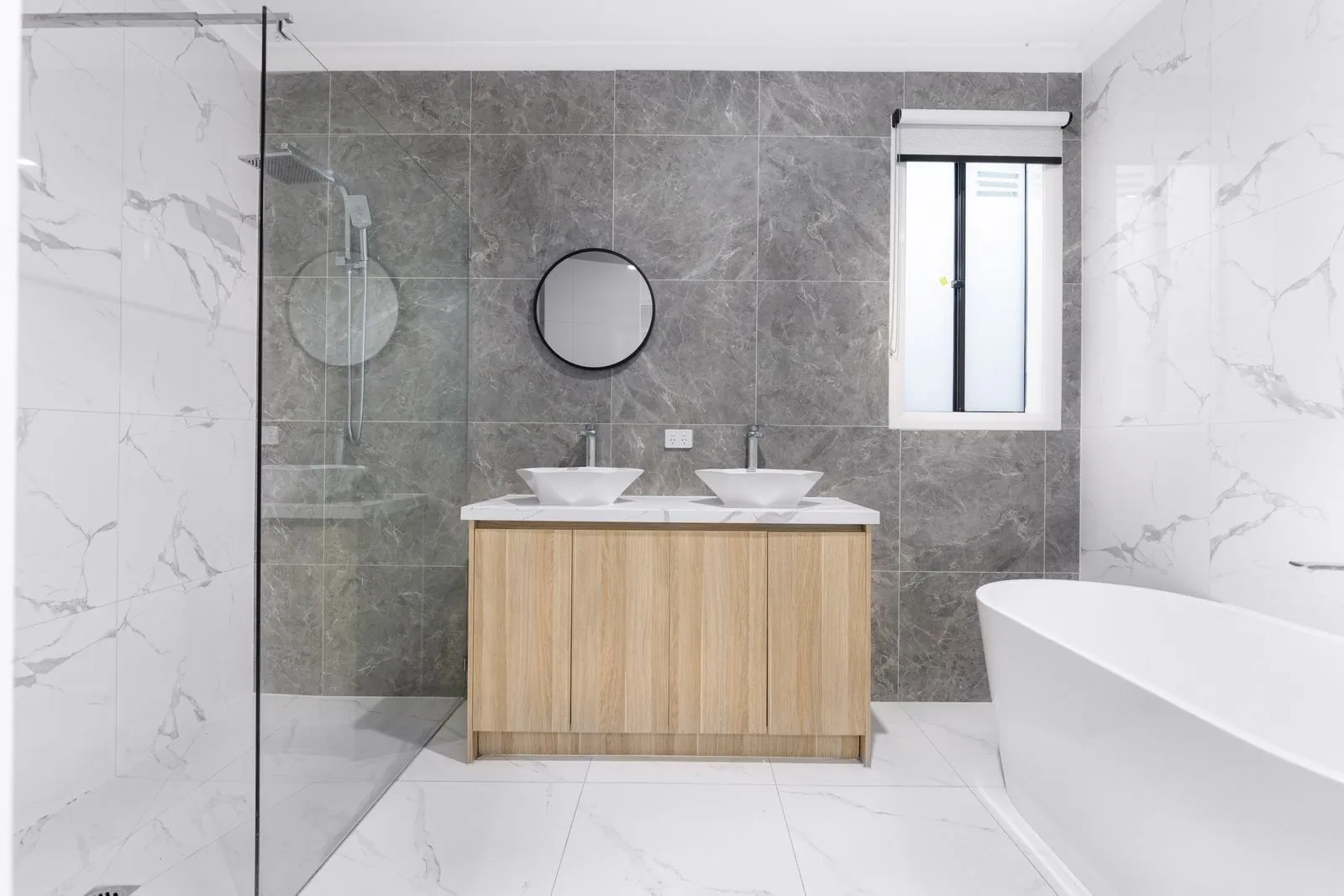 A calm family bathroom with marble walls, timber joinery and a freestanding bath in Floreat